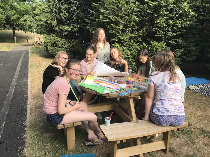Grupo de meninas sentadas no banco de madeira ao ar livre na colónia de férias em Inglês