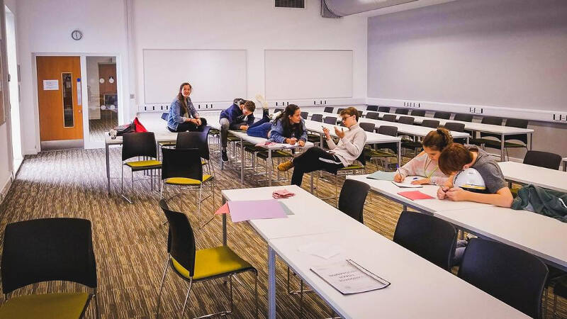 Jovens na sala de aula em atividade de grupo nas secretárias da colónia de férias em Inglês