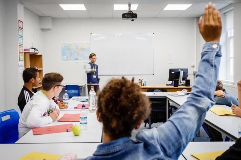 Criança no quadro da sala de aula e outras sentadas nas mesas a participar em atividade do campo de férias internacional