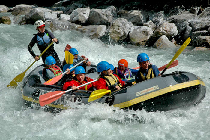 Crianças e monitor no barco a descer o rio na atividade de rafting do campo de férias desportos aquáticos