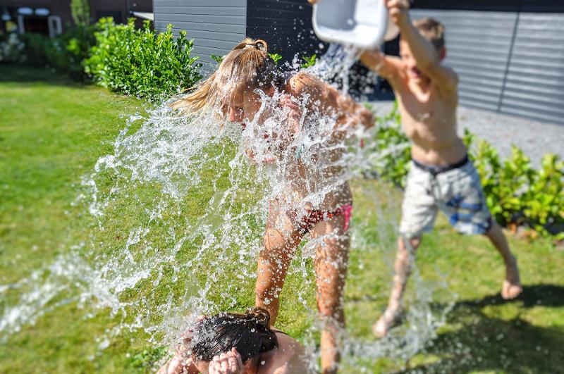 Menino a molhar menina participante com um balde de água num jogo de grupo do campo de férias 