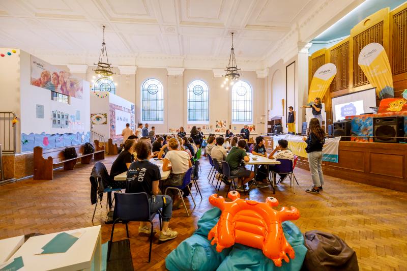 Jovens separados por grupos em mesas durante a aula teórica de inglês no campo de férias Inglaterra