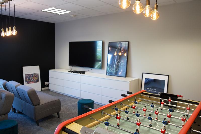Sala de convívio com televisão e uma mesa de matraquilhos do campo de férias de futebol