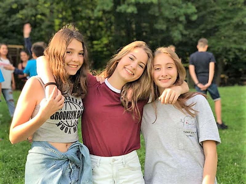Três meninas a sorrir abraçadas em tempo livre do campo de férias