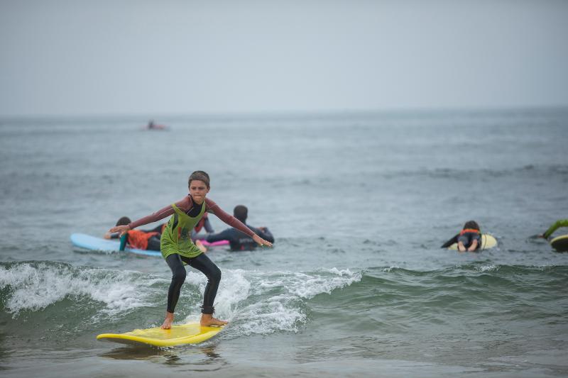 Criança na prancha de surf a apanhar uma onda durante o campo de férias