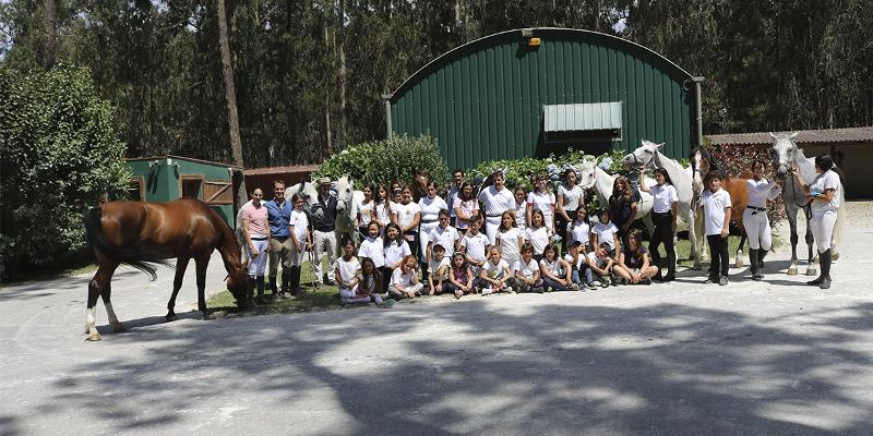 Foto de grupo no jardim com cavalos e crianças participantes do campo de férias de equitação