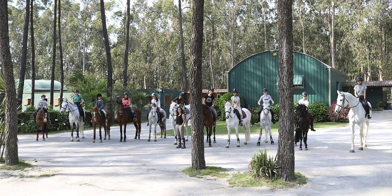 Participantes montados a cavalo com a instrutora de equitação no campo de férias equestre