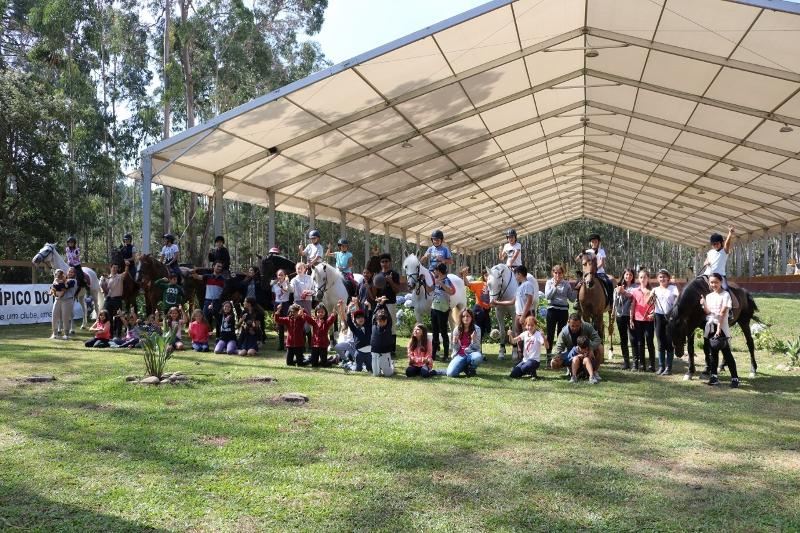 Foto de grupo das crianças no campo de férias com alguns participantes montados a cavalo