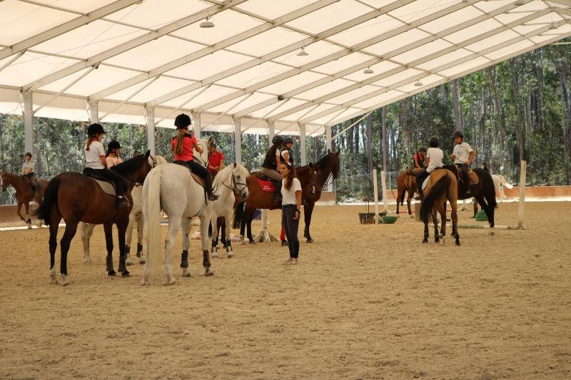 Instrutora de equitação a falar para os meninos que estão montados no cavalo no campo de férias de equitação em Portugal