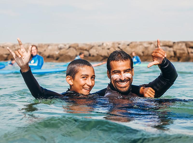 Criança e instrutor felizes no mar durante os campos de ferias com reserva antecipada