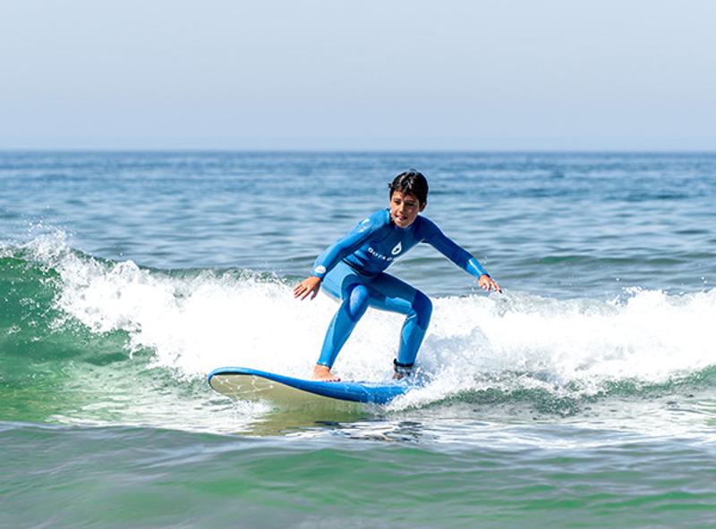 Menino a surfar uma onda na zona de rebentação durante o campo de férias de surf 