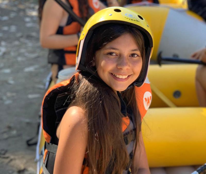 Menina a sorrir equipada com capacete e colete salva-vidas no campo de férias