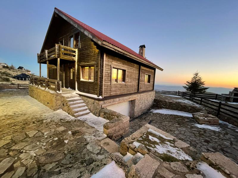  Na imagem, vê-se um chalé de madeira acolhedor, rodeado por neve e montanhas, com o pôr do sol a iluminar o céu. Este cenário no campo de férias serra da estrela é perfeito para relaxar e conectar-se com a natureza.