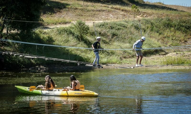 Jovens a fazer ponte de cordas e canoagem no rio no campo de férias