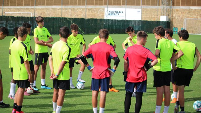 Jogadores no relvado a ouvir as indicações do treinador no campo de férias de futebol