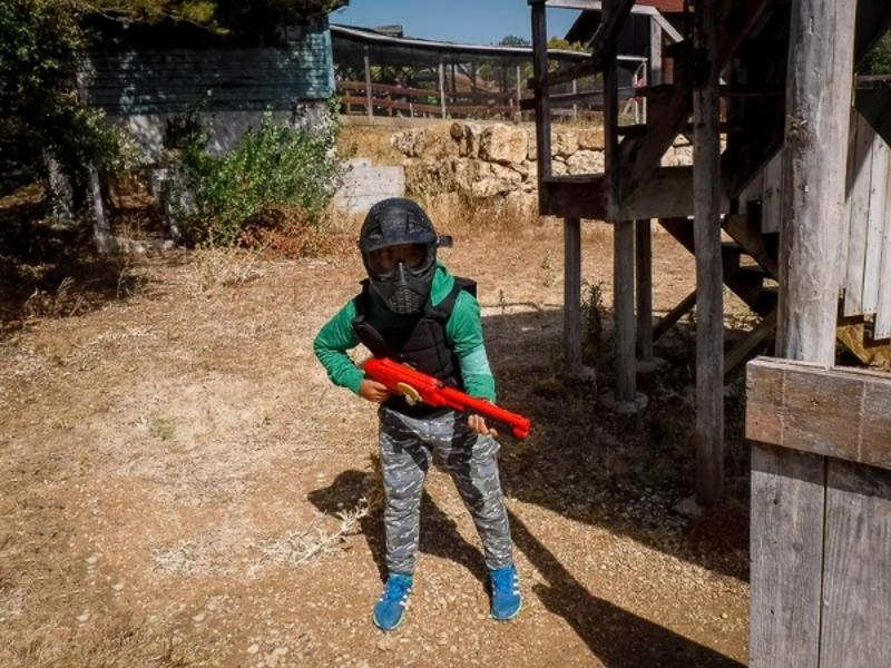 Criança totalmente equipada a jogar paintball no campo de férias