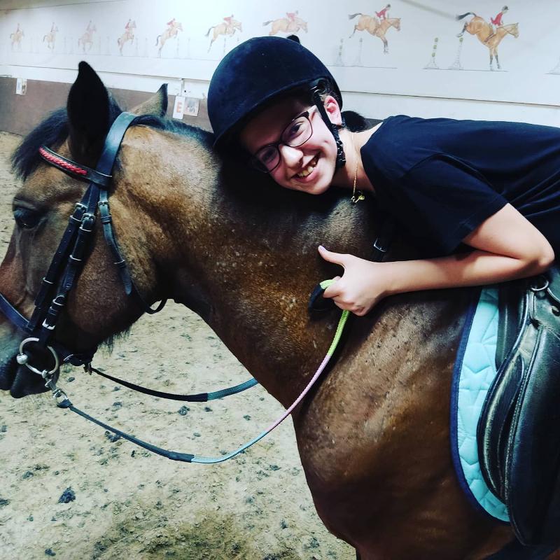 Menina a sorrir montada e abraçada no campo de férias com cavalos