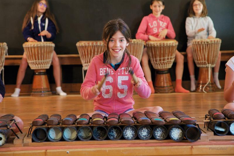 Menina a sorrir a tocar instrumento de percussão no campo de férias música