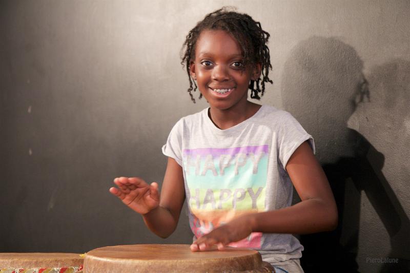 Menina a sorrir enquanto toca djembe no campo de férias música