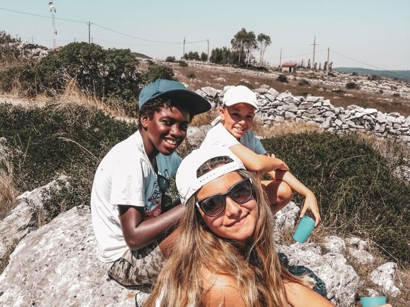 Três crianças sorridentes sentadas nas pedras durante o tempo livre do campo de férias Santarém