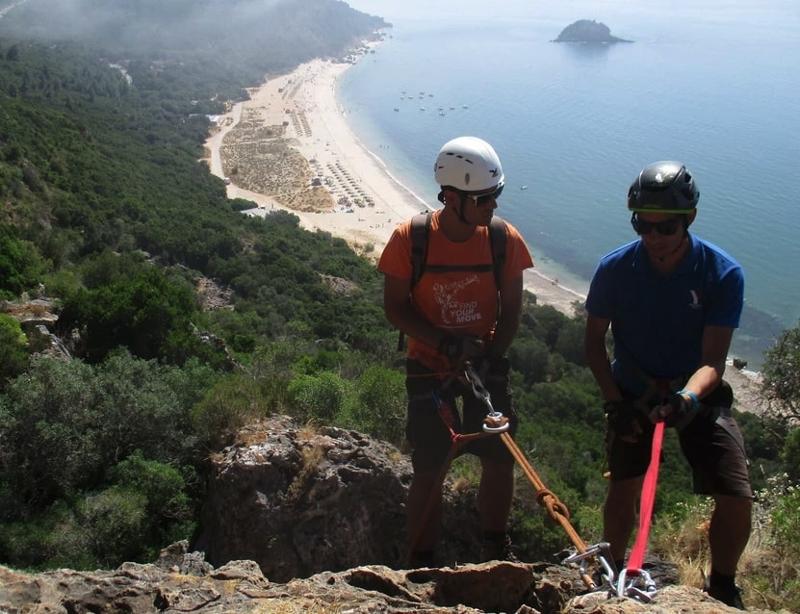 Jovens a fazer rappel na serra da arrábida com vista para uma praia de Setúbal