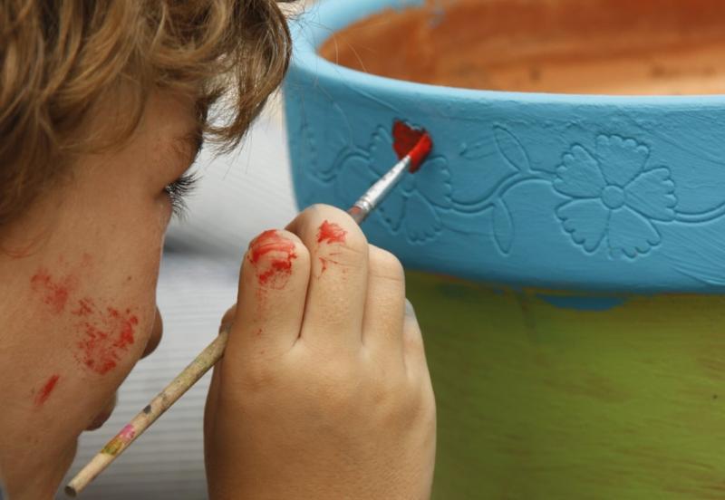 Menino a pintar um vaso com tinta e pincel durante o campo de férias Natal
