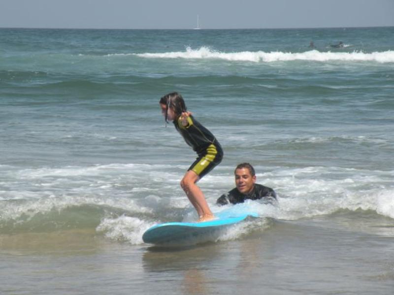 Instrutor a empurrar a prancha da menina que está a fazer surf na zona de rebentação no campo de férias Lisboa