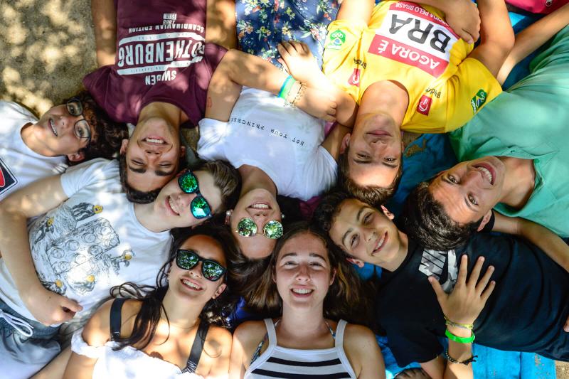 Jovens deitados no chão em roda a olhar para cima a sorrirem de felicidade no campo de férias perto de Lisboa