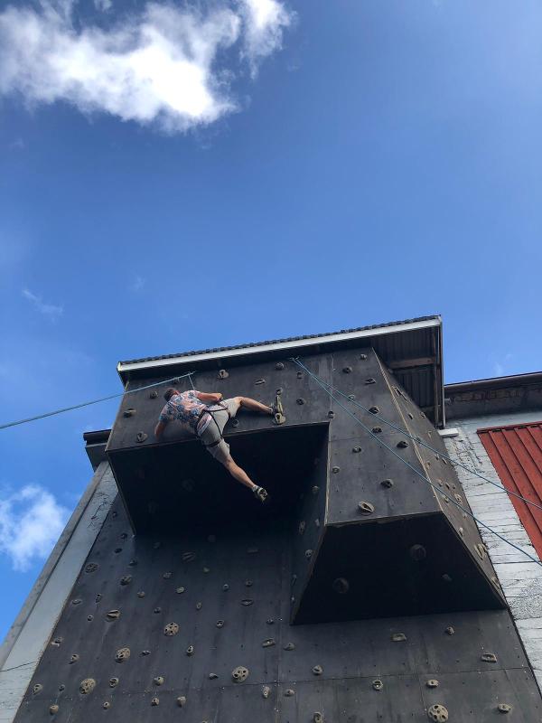 menino no topo da parede de escalada no campo de férias