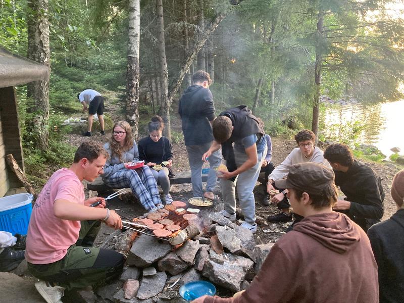 participantes a cozinhar hambúrgueres para o almoço na fogueira no meio da natureza do campo de férias