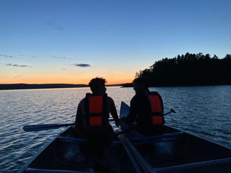 dois participantes a ver o pôr-do-sol na canoa no meio do lago do campo de férias na Suécia