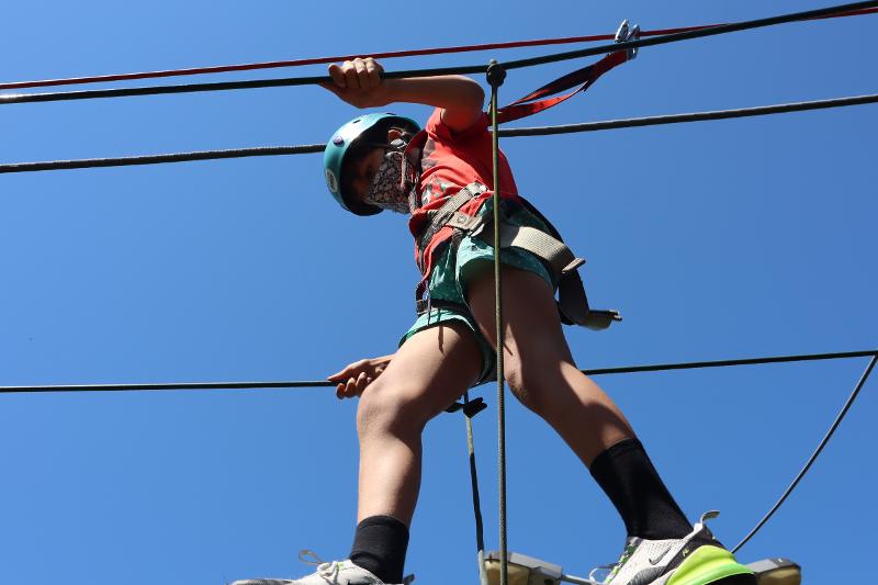 Menino a atravessar uma ponte de cordas devidamente equipado no campo de férias no Porto