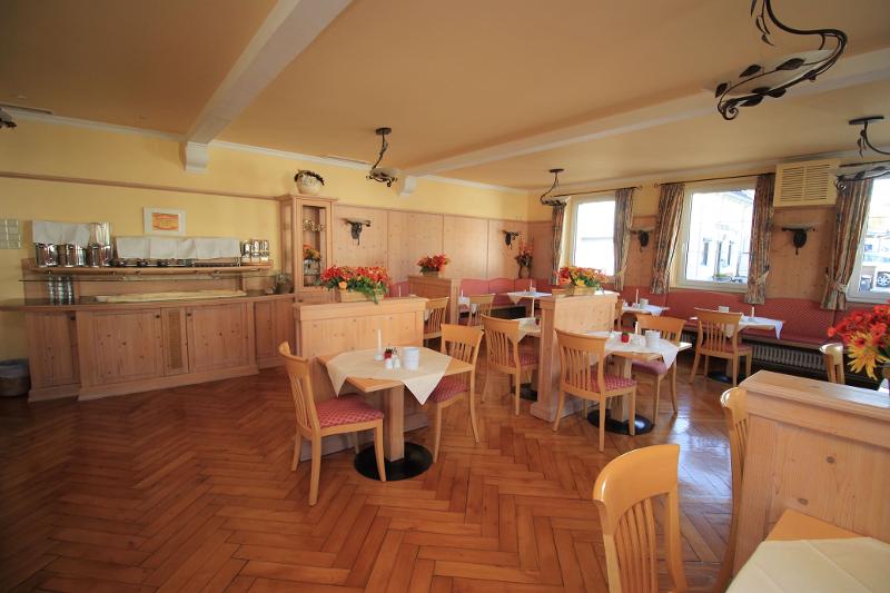 Uma sala de jantar acolhedora com mesas e cadeiras de madeira, decorada com flores e luz natural, oferece um ambiente agradável para refeições durante o curso de línguas.