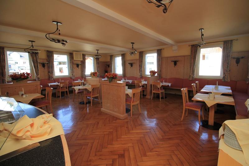 Uma sala de jantar espaçosa e luminosa com mesas de madeira, decorada com flores, oferece um ambiente acolhedor para refeições durante o curso de línguas na Alemanha.