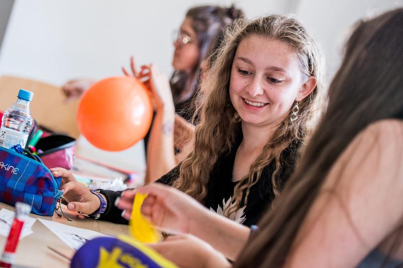Uma jovem sorri enquanto participa numa atividade em grupo com outros estudantes, num ambiente de aprendizagem descontraído durante o curso de línguas na Alemanha.