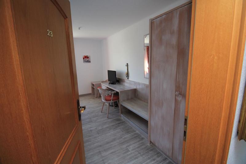 Quarto simples e bem organizado, com uma secretária e armário de madeira, ideal para estudo e descanso durante o curso de línguas estrangeiras.