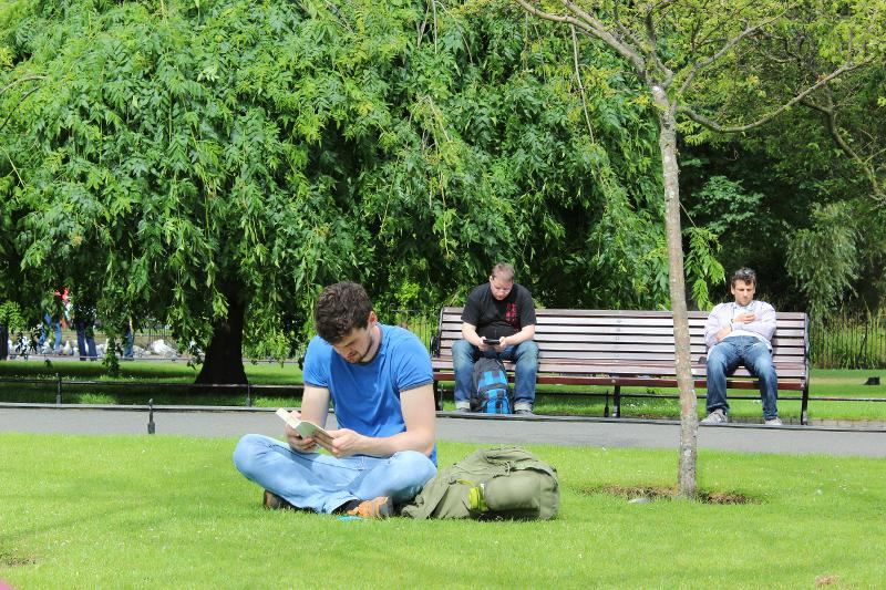 participante do curso de ingles em dublin a ler um livro sentado na relva da universidade