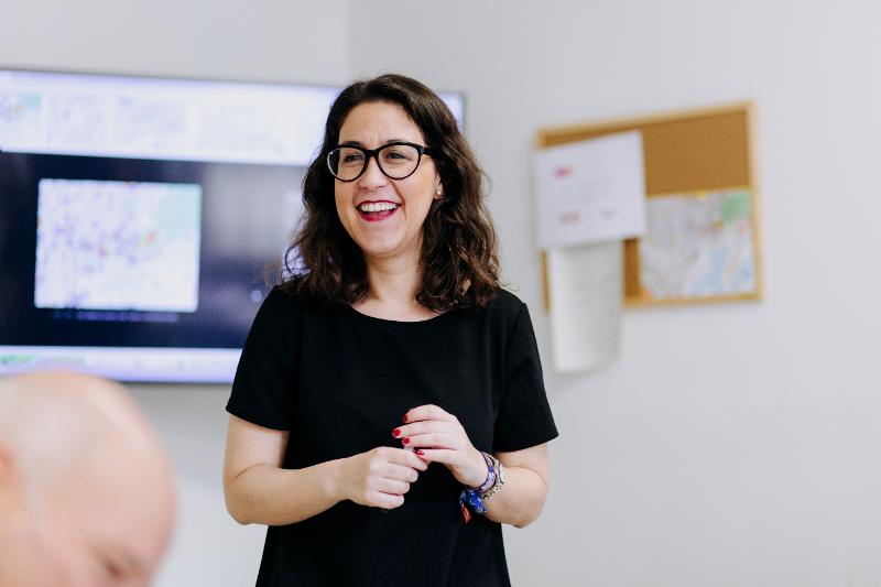 Professora sorridente a conduzir uma aula de curso de espanhol com entusiasmo.