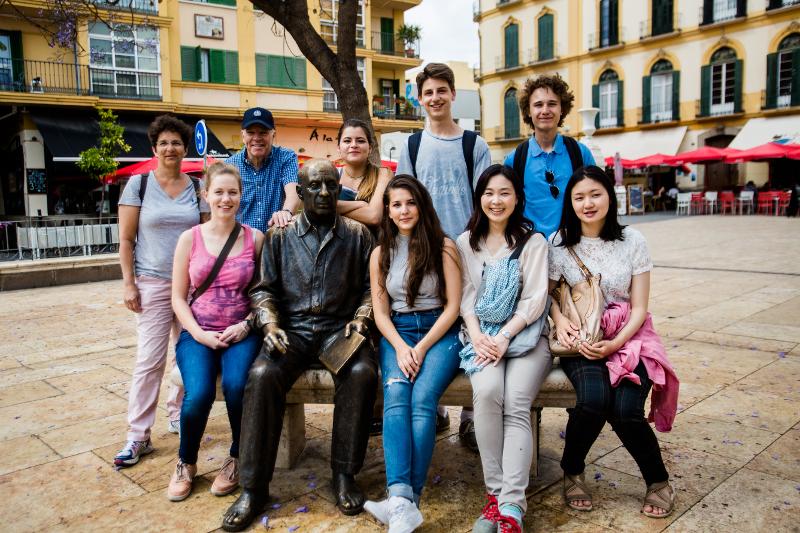 Grupo de estudantes de um curso de espanhol a tirar uma foto junto a uma estátua numa praça histórica