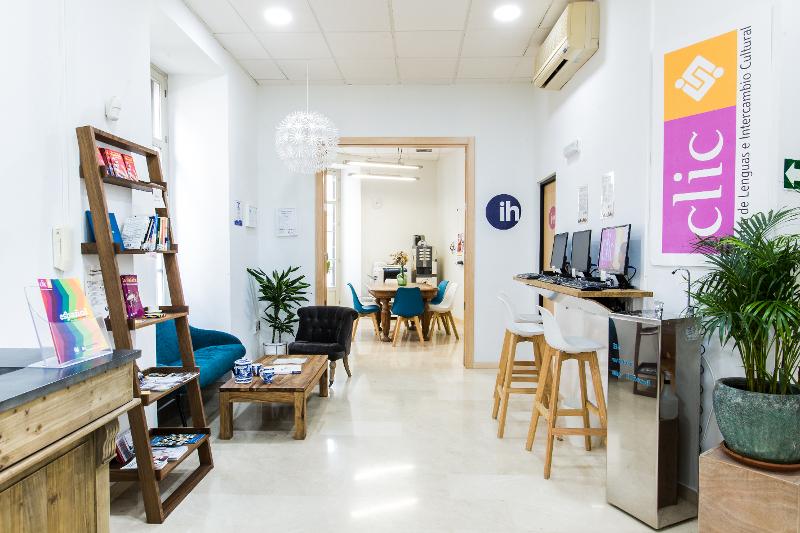 Entrada acolhedora de uma escola de cursos de espanhol, com espaço de leitura e computadores.