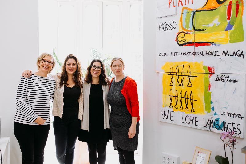 Quatro professoras de um curso de línguas a sorrirem juntas numa sala iluminada e acolhedora
