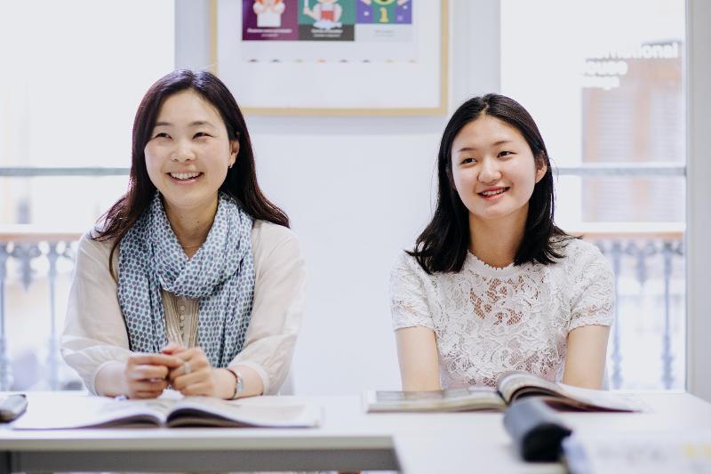 Duas estudantes sorridentes a participar num curso de línguas numa sala iluminada