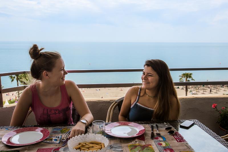 Duas estudantes de um curso de línguas a desfrutar de uma refeição numa varanda com vista para o mar