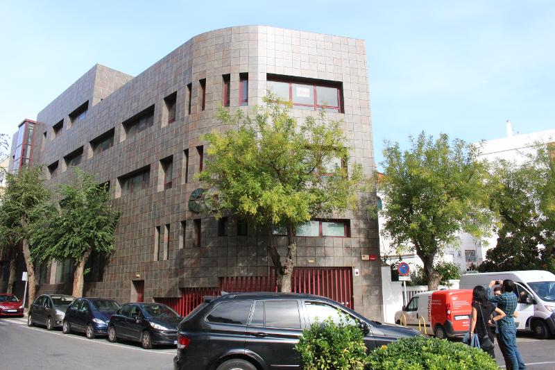 Fachada moderna do edifício dos cursos de língua espanhola, rodeado de árvores numa rua tranquila.