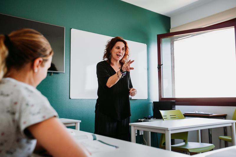 Professora a ensinar numa aula dos cursos de língua espanhola, com uma aluna atenta.