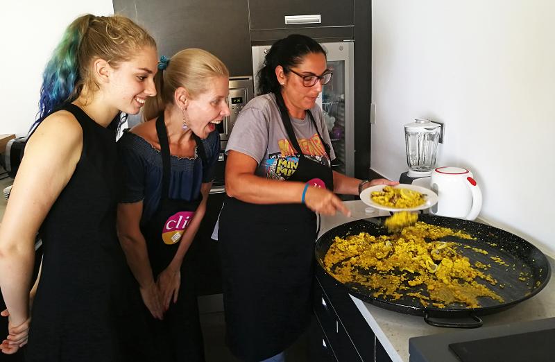 Alunas entusiasmadas observam uma cozinheira a preparar um prato típico numa aula prática dos cursos de língua espanhola.