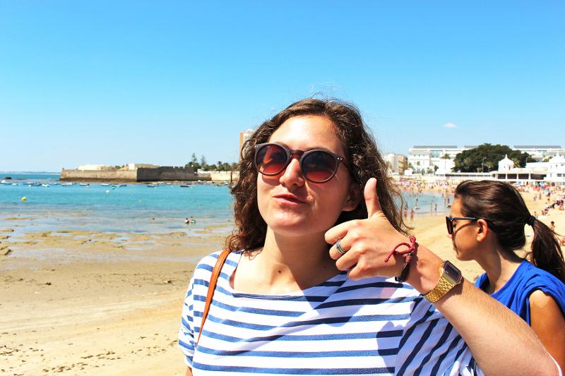 Aluna dos cursos de língua espanhola a desfrutar de um dia de sol na praia com um sinal de aprovação.