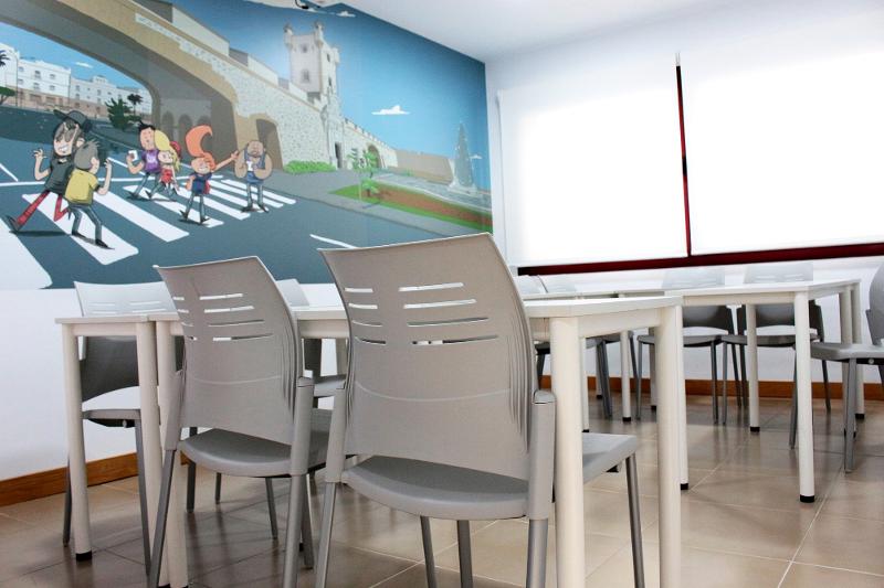 Sala de aula dos cursos de língua espanhola, equipada com mesas e cadeiras, com uma parede decorada com uma ilustração.