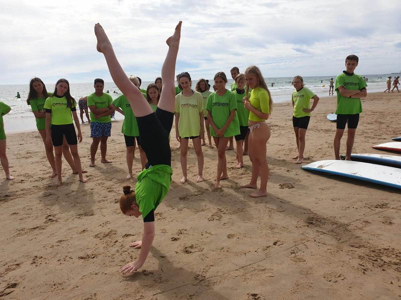 Grupo de jovens dos cursos de espanhol na praia, a assistir a uma demonstração de acrobacias.