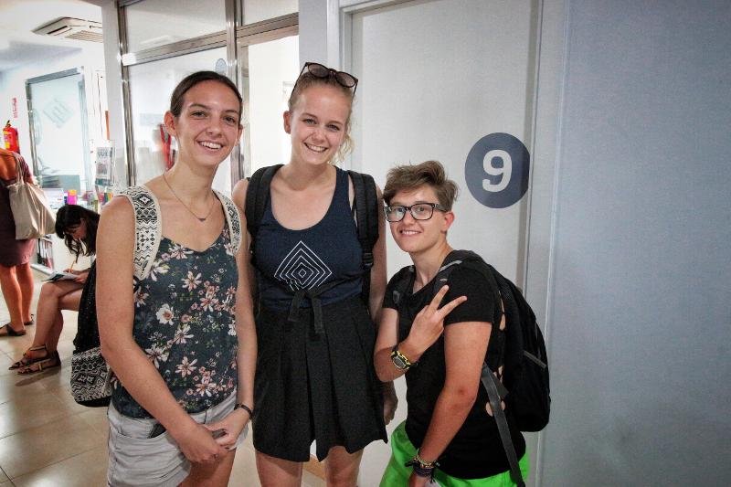 Três alunos dos cursos de espanhol a sorrir no corredor, prontos para a aula.